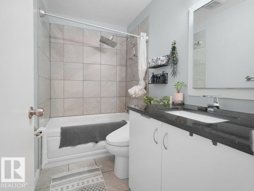 Bathroom featuring a white vanity with dark countertop, undermount sink, contemporary faucet, and a large wall-mounted mirror - #54 2131 Oak St, Sherwood Park, AB - Indoor Photo Showing Bathroom