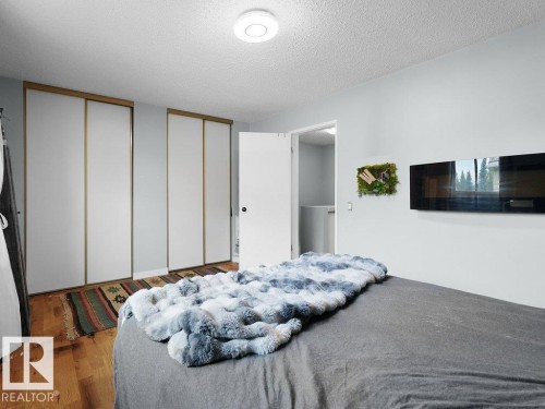 Wood-finish flooring, built-in sliding panel closets, and a wall-mounted electric fireplace - #54 2131 Oak St, Sherwood Park, AB - Indoor Photo Showing Bedroom