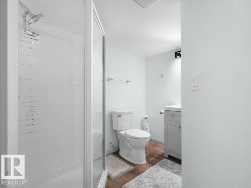 Glass-enclosed shower with a multi-function showerhead, white toilet, wood-finish flooring, and a vanity with a white countertop - #54 2131 Oak St, Sherwood Park, AB - Indoor Photo Showing Bathroom