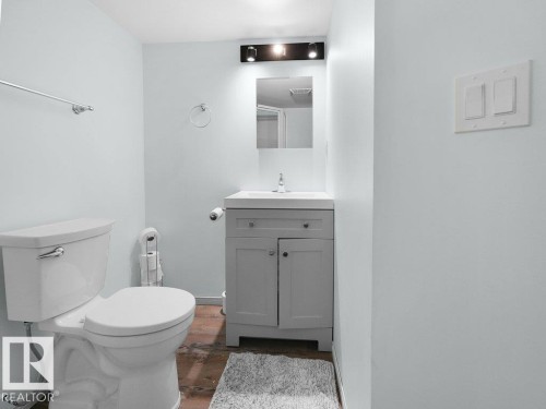 White porcelain toilet, gray vanity with integrated sink, chrome faucet, and rectangular mirror with overhead lighting - #54 2131 Oak St, Sherwood Park, AB - Indoor Photo Showing Bathroom