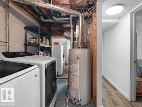 Utility area featuring exposed overhead plumbing, a visible water heater, and wood-finish flooring in an adjacent space - #54 2131 Oak St, Sherwood Park, AB - Indoor Photo Showing Basement