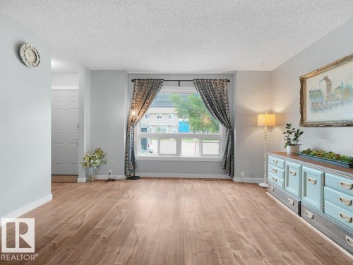 Wood-finish flooring throughout, bright window with white trim, light-toned walls, and a white front door - #54 2131 Oak St, Sherwood Park, AB - Indoor Photo Showing Other Room