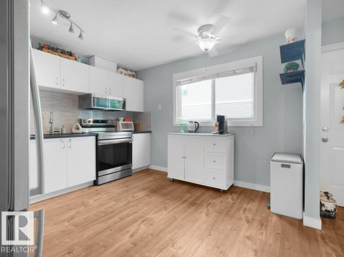 Kitchen featuring white cabinetry, wood-finish flooring, stainless steel appliances, and a tile backsplash - #54 2131 Oak St, Sherwood Park, AB - Indoor Photo Showing Kitchen