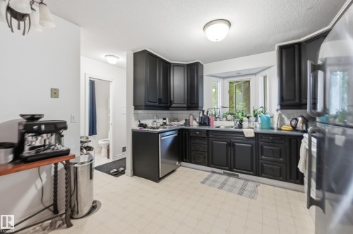 Kitchen featuring black cabinetry, stainless steel dishwasher, light-toned flooring, and a bay window - 14631 Summit Drive Nw, Edmonton, AB 