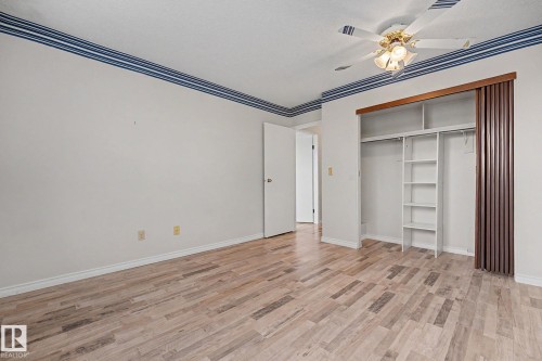 Spacious room featuring wood-finish flooring, a built-in closet with shelving and hanging rods, and a ceiling fan with integrated lighting - 1096 Knottwood Road Nw, Edmonton, AB - Indoor Photo Showing Other Room