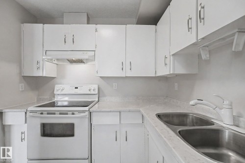 Bright kitchen featuring white cabinetry, a white electric range, and a double basin stainless steel sink with a white faucet - 1096 Knottwood Road Nw, Edmonton, AB - Indoor Photo Showing Kitchen With Double Sink