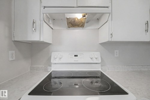 White electric range with a black smooth cooktop, complemented by white upper cabinetry with brushed nickel hardware, and stone-look countertops - 1096 Knottwood Road Nw, Edmonton, AB - Indoor Photo Showing Laundry Room