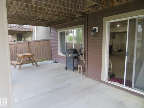 Concrete patio with a wood privacy fence, featuring a sliding glass door and an exterior wall light fixture - 3233 Winspear Crescent Sw, Edmonton, AB - Outdoor With Deck Patio Veranda With Exterior