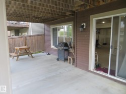 Concrete patio with a wood privacy fence, featuring a sliding glass door and an exterior wall light fixture - 