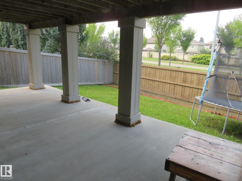 Covered concrete patio with supporting columns and a wooden privacy fence bordering a grass lawn - 3233 Winspear Crescent Sw, Edmonton, AB - Outdoor With Deck Patio Veranda With Exterior