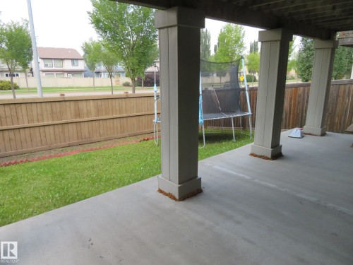 Concrete patio with supportive columns, bordered by a wooden fence and a strip of green lawn - 3233 Winspear Crescent Sw, Edmonton, AB - Outdoor With Exterior