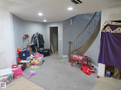 Recessed lighting illuminates a carpeted floor, complemented by a staircase featuring wood-finish handrails and black metal spindles - 3233 Winspear Crescent Sw, Edmonton, AB - Indoor