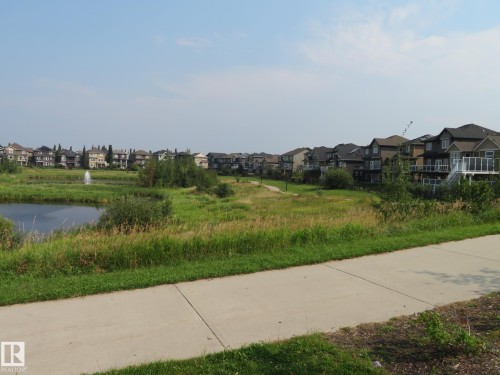 Paved pathway bordering a naturalized pond with a water feature, surrounded by established homes and mature landscaping - 3233 Winspear Crescent Sw, Edmonton, AB - Outdoor With View