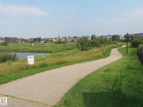 Paved pathway paralleling a water feature, with established residential structures in the background - 3233 Winspear Crescent Sw, Edmonton, AB - Outdoor With View