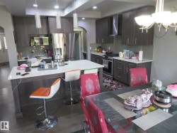 Contemporary kitchen featuring wood-finish cabinetry, stainless steel appliances, a center island with a sink, and pendant lighting - 