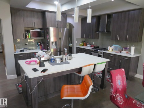 Modern kitchen featuring wood-finish cabinetry, stainless steel appliances, a center island with a light-toned countertop, and pendant lighting - 3233 Winspear Crescent Sw, Edmonton, AB - Indoor Photo Showing Kitchen
