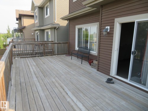 Spacious outdoor deck with wood railing, leading to a sliding glass patio door and an exterior wall light fixture - 3233 Winspear Crescent Sw, Edmonton, AB - Outdoor With Deck Patio Veranda With Exterior