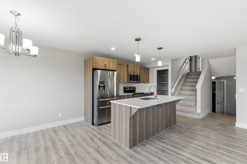 Open-concept kitchen with wood-finish flooring, stainless steel appliances, and a central island featuring a white countertop - 7 Mclean Court, Leduc, AB - Indoor Photo Showing Kitchen With Stainless Steel Kitchen