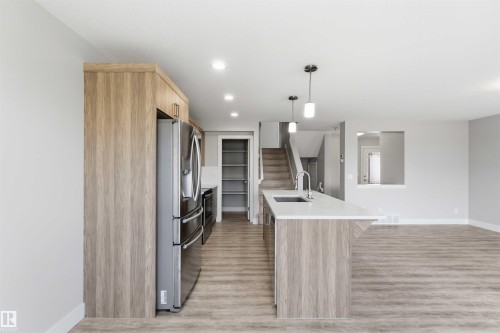 Open-concept kitchen featuring wood-finish cabinetry, stainless steel appliances, a center island with a sink, and pendant lighting - 7 Mclean Court, Leduc, AB - Indoor Photo Showing Kitchen