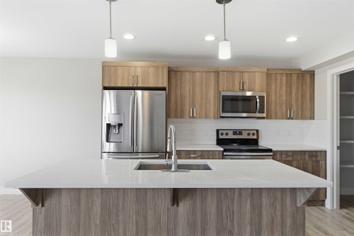 Kitchen featuring wood-finish cabinetry, stainless steel appliances, white subway tile backsplash, and a central island with a sink and white countertop - 7 Mclean Court, Leduc, AB - Indoor Photo Showing Kitchen With Stainless Steel Kitchen With Double Sink With Upgraded Kitchen
