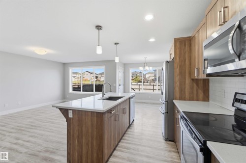 Kitchen featuring wood-finish cabinetry, stainless steel appliances, white subway tile backsplash, and an island with a stainless steel sink and pendant lighting - 7 Mclean Court, Leduc, AB - Indoor Photo Showing Kitchen With Upgraded Kitchen