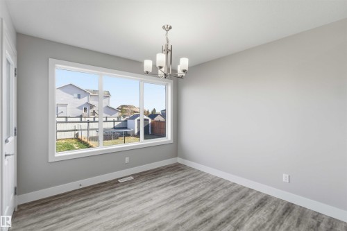 Expansive window offering abundant natural light, brushed nickel chandelier with frosted glass shades, wood-finish flooring, and crisp white trim details - 7 Mclean Court, Leduc, AB - Indoor Photo Showing Other Room