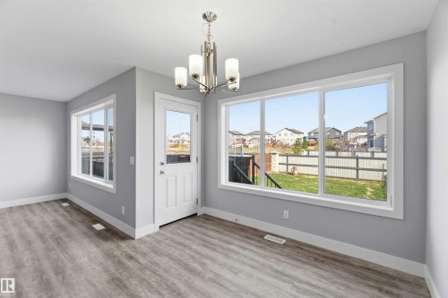 Wood-finish flooring, white trim, multiple windows, a glass-panel exterior door, and a contemporary chandelier - 7 Mclean Court, Leduc, AB - Indoor Photo Showing Other Room