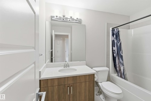 Bathroom featuring a wood-finish vanity with a white countertop, an integrated sink, a large wall mirror, and a shower-tub combination - 7 Mclean Court, Leduc, AB - Indoor Photo Showing Bathroom