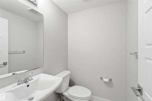 Pedestal sink with chrome faucet, wall-mounted mirror, overhead lighting, and white toilet - 7 Mclean Court, Leduc, AB - Indoor Photo Showing Bathroom