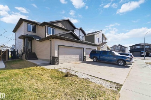 Two-story residence featuring light-toned siding with dark trim accents, a two-car garage with a stone veneer base, a covered front entry with dark wood stairs, and a concrete driveway - 7 Mclean Court, Leduc, AB - Outdoor With Facade