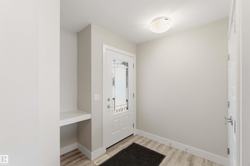 Entryway featuring a white door with decorative glass inserts, wood-finish flooring, and a built-in shelf - 7 Mclean Court, Leduc, AB - Indoor Photo Showing Other Room