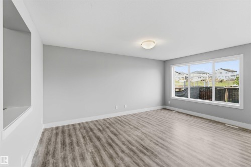Spacious room with wood-finish flooring, a large multi-pane window, flush-mount ceiling light, and neutral wall paint - 7 Mclean Court, Leduc, AB - Indoor Photo Showing Other Room