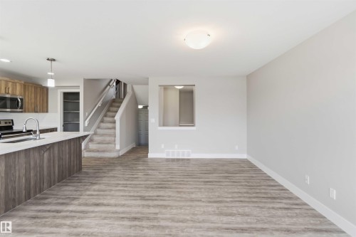 Wood-finish flooring, staircase with carpeted treads, built-in shelving, kitchen island with sink, and stainless steel appliances - 7 Mclean Court, Leduc, AB - Indoor Photo Showing Kitchen