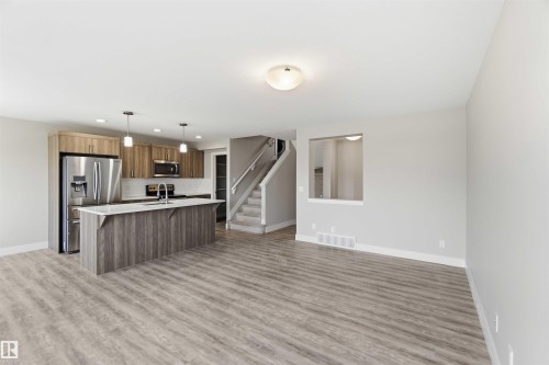 Modern kitchen featuring wood-finish cabinetry, stainless steel appliances, a center island with countertop, and pendant lighting - 7 Mclean Court, Leduc, AB - Indoor Photo Showing Kitchen