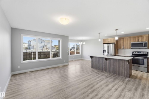 Open-concept living space featuring wood-finish flooring, a kitchen island with pendant lighting, stainless steel appliances, and wood-finish cabinetry - 7 Mclean Court, Leduc, AB - Indoor Photo Showing Kitchen With Stainless Steel Kitchen