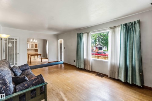 Hardwood-finish flooring, large picture window, arched doorways, and white painted walls - 11710 94 Street Nw, Edmonton, AB - Indoor Photo Showing Living Room