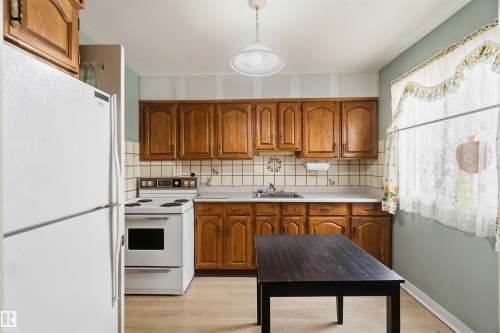 Kitchen featuring wood cabinetry, a white electric range, and a single-basin sink with a tile backsplash - 11710 94 Street Nw, Edmonton, AB - Indoor Photo Showing Kitchen
