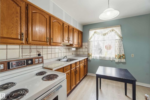 Wood-finish cabinetry paired with a tile backsplash, durable countertops, and a stainless steel sink - 11710 94 Street Nw, Edmonton, AB - Indoor Photo Showing Kitchen