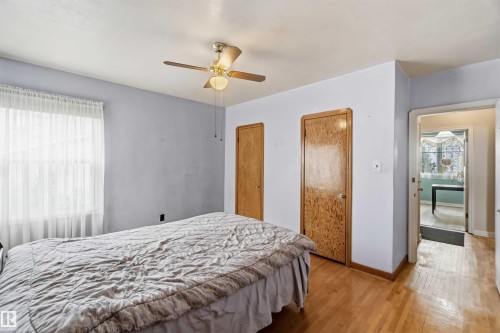 Hardwood flooring throughout, ceiling fan with integrated lighting, natural wood doors, and a window with sheer coverings - 11710 94 Street Nw, Edmonton, AB - Indoor Photo Showing Bedroom