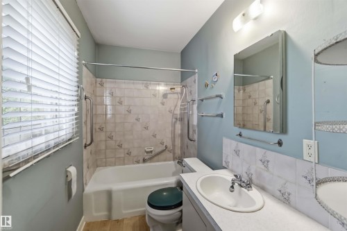 Bathtub shower combination with tiled surround, single vanity with integrated sink, and wood-finish flooring - 11710 94 Street Nw, Edmonton, AB - Indoor Photo Showing Bathroom