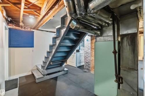Exposed ceiling joists with visible wiring, industrial-style staircase, brick accent wall, laundry appliances, and rubber flooring - 11710 94 Street Nw, Edmonton, AB - Indoor Photo Showing Basement