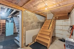 Unfinished basement with exposed concrete walls, wood-framed ceiling, and a wooden staircase with a black handrail - 