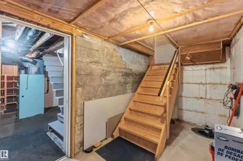 Unfinished basement with exposed concrete walls, wood-framed ceiling, and a wooden staircase with a black handrail - 11710 94 Street Nw, Edmonton, AB - Indoor Photo Showing Basement