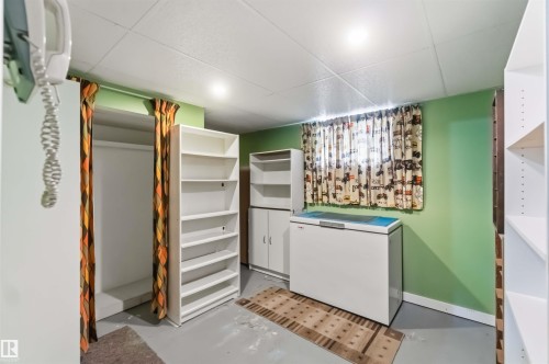 Utility room featuring white built-in cabinetry with shelving, a front-load washer/dryer unit, bright green accent walls, recessed ceiling lighting, and wood-finish flooring with a decorative border detail - 11710 94 Street Nw, Edmonton, AB - Indoor