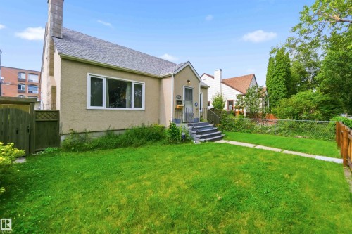 Stucco exterior with a peaked roofline, multi-pane windows, front entry stairs, and a front yard with a concrete pathway - 11710 94 Street Nw, Edmonton, AB - Outdoor