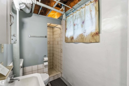 Bathroom featuring a walk-in shower with tile surround and glass enclosure, pedestal sink, and skylight providing natural illumination - 11710 94 Street Nw, Edmonton, AB - Indoor Photo Showing Bathroom