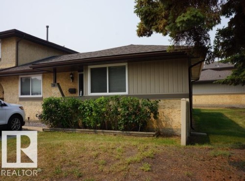 Stucco and vertical siding exterior with white window frames, dark gutters, and a planted shrub bed - #38 8930 99 Av, Fort Saskatchewan, AB - Outdoor
