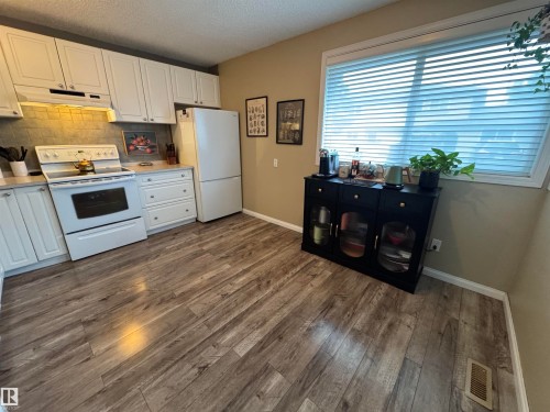 Updated kitchen featuring white cabinetry, a tile backsplash, white appliances, and wood-finish flooring - #38 8930 99 Av, Fort Saskatchewan, AB - Indoor Photo Showing Kitchen