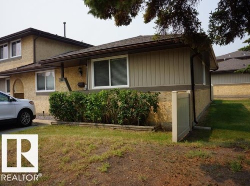 Neutral exterior with stucco and vertical siding, featuring white-framed windows and a dark shingle roof - #38 8930 99 Av, Fort Saskatchewan, AB - Outdoor