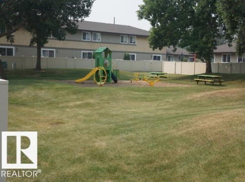 Expansive green space featuring playground equipment, a picnic table, and mature trees - #38 8930 99 Av, Fort Saskatchewan, AB - Outdoor